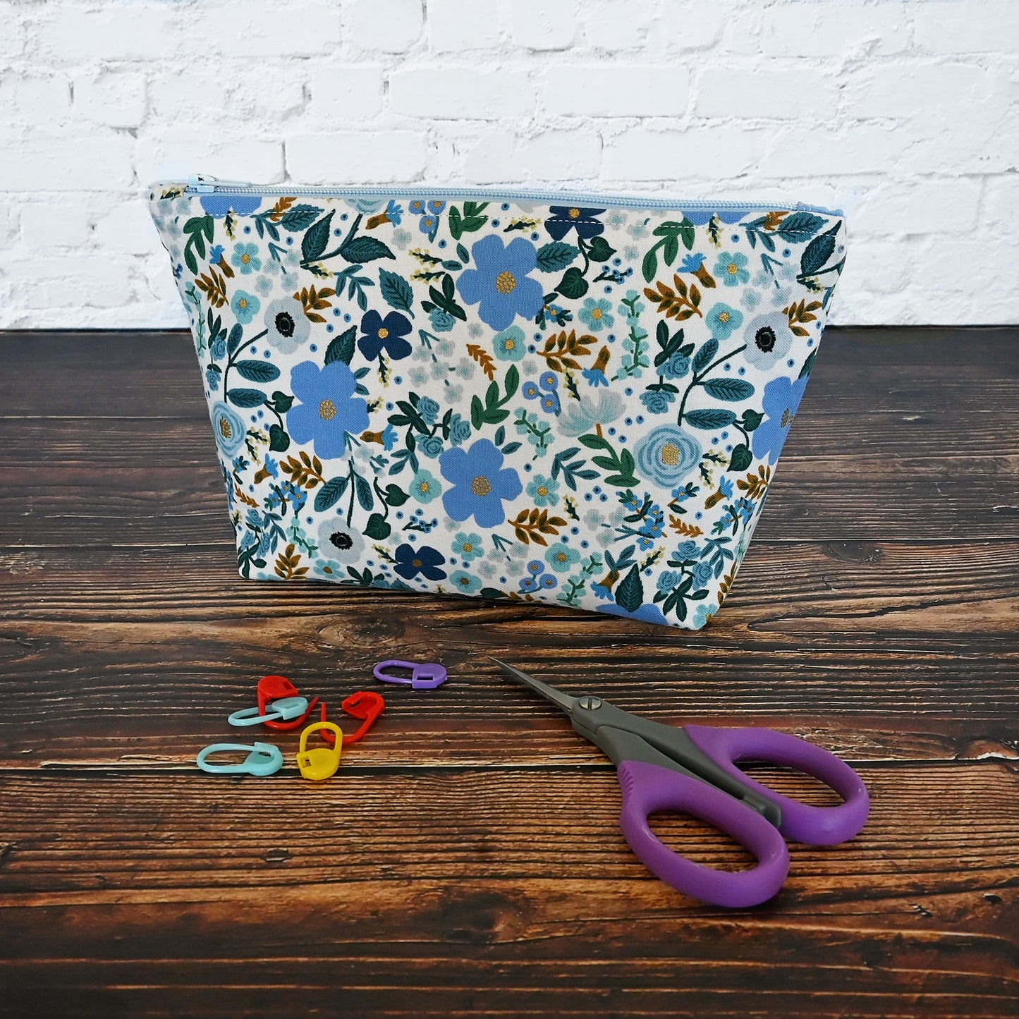 Pretty blue floral accessory pouch in fabric from Rifle Paper Co. This pouch features a blue floral with small gold metallic details, and is lined in a blue and white fabric. It closes securely with a pretty blue zipper. Great for all of your acessories!
