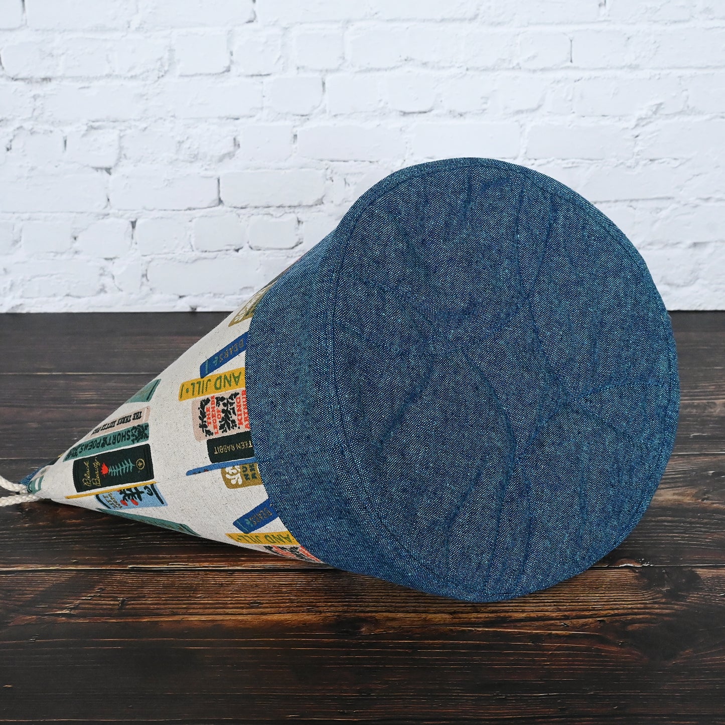 Bucket bag for knitting or crochet made from Rilfe Paper's Book Club Canvas and paired with a peacock linen from Robert Kaufman. Made with multiple pockets and a double drawstring closure. Made in Canada by Yellow Petal Handmade.