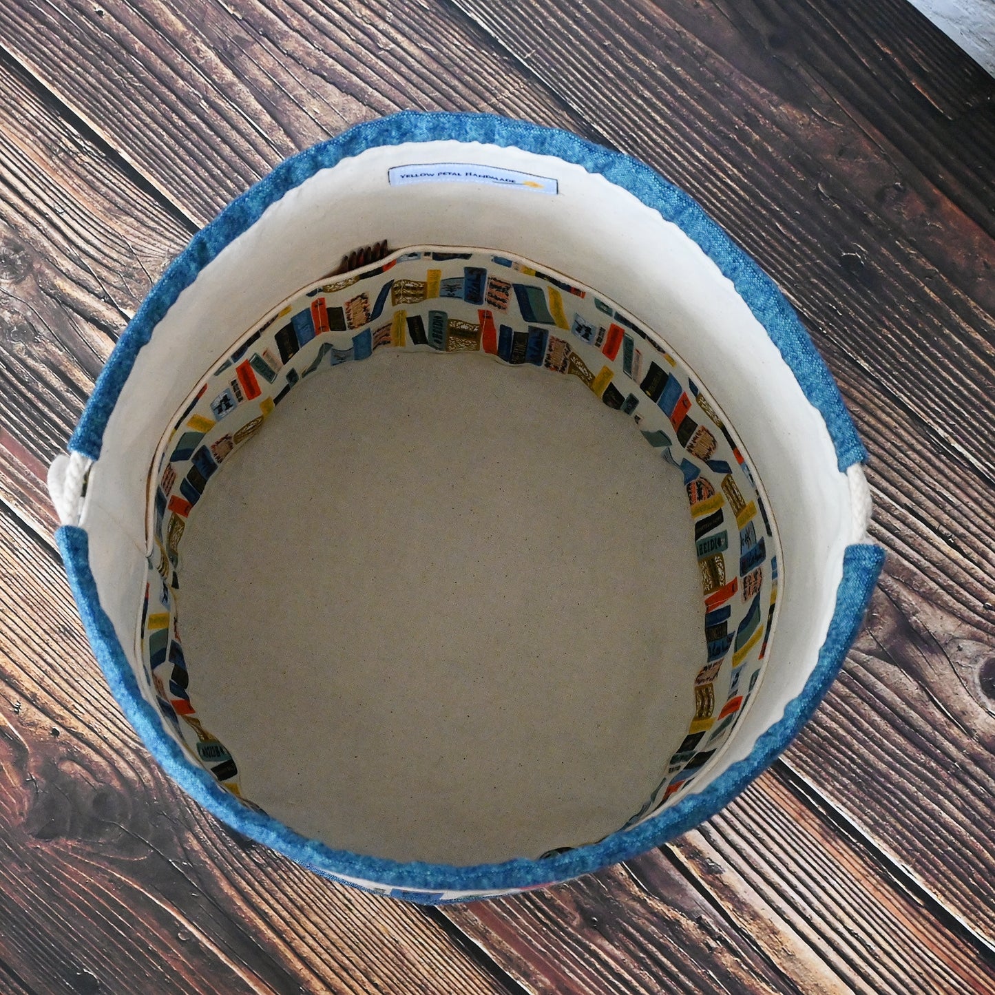 Bucket bag for knitting or crochet made from Rilfe Paper's Book Club Canvas and paired with a peacock linen from Robert Kaufman. Made with multiple pockets and a double drawstring closure. Made in Canada by Yellow Petal Handmade.