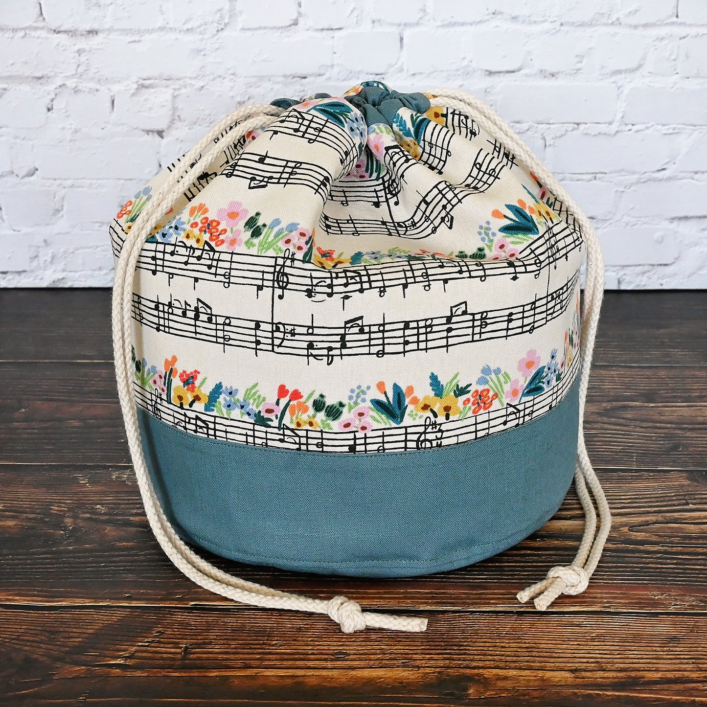 Fun Bucket Bag for knitting and crochet projects.  Features Music Notes Canvas by Rifle Paper Co paired with a steel blue linen.  Equipped with multiple interior pockets and a drawstring closure.  Made in Canada by Yellow Petal Handmade.