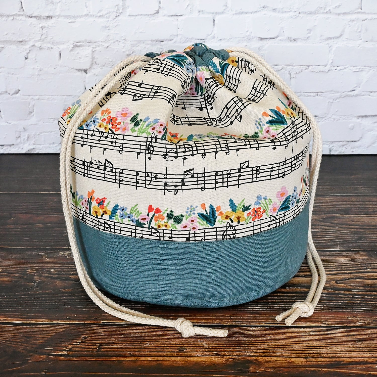 Fun Bucket Bag for knitting and crochet projects.  Features Music Notes Canvas by Rifle Paper Co paired with a steel blue linen.  Equipped with multiple interior pockets and a drawstring closure.  Made in Canada by Yellow Petal Handmade.